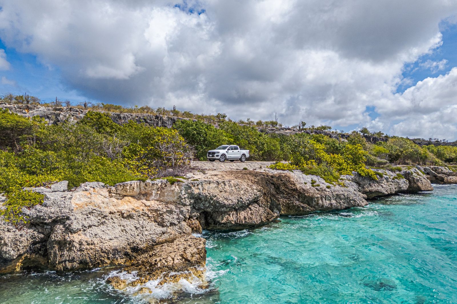 White Ford Ranger on a coastal road above turquoise water